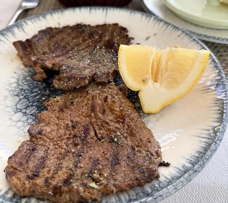 Two grilled steaks with a lemon wedge on a blue-rimmed plate
