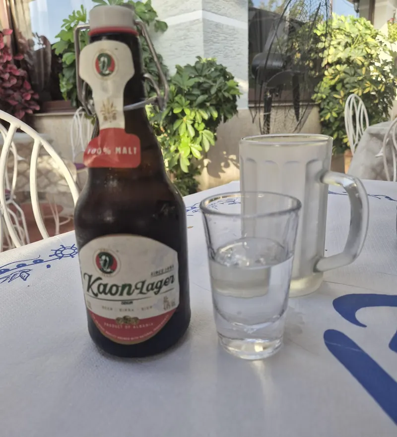 A small glass of rakia beside a bottle of Kaon lager on a white tablecloth
