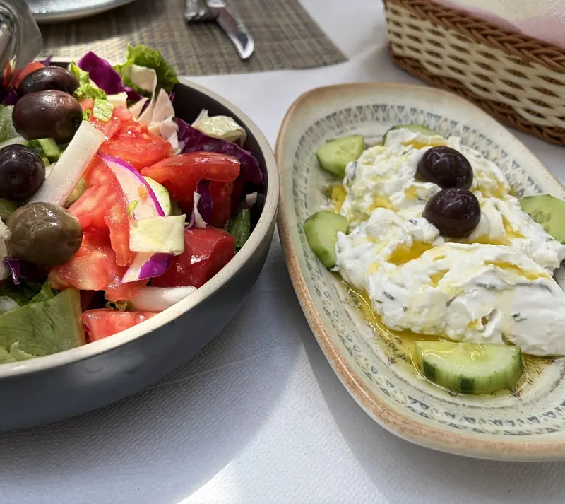 Village salad with olives beside a plate of yogurt sauce with cucumber