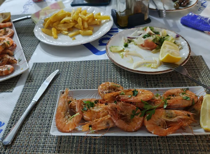 A table with grilled shrimp, fried potatoes, salad and lemon