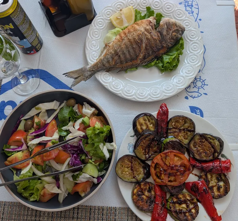 From above: grilled sea bream, a mixed salad and a plate of grilled vegetables on a white tablecloth