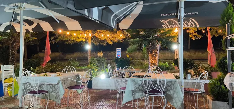 The terrace after dark, string lights in the trees beyond the umbrellas