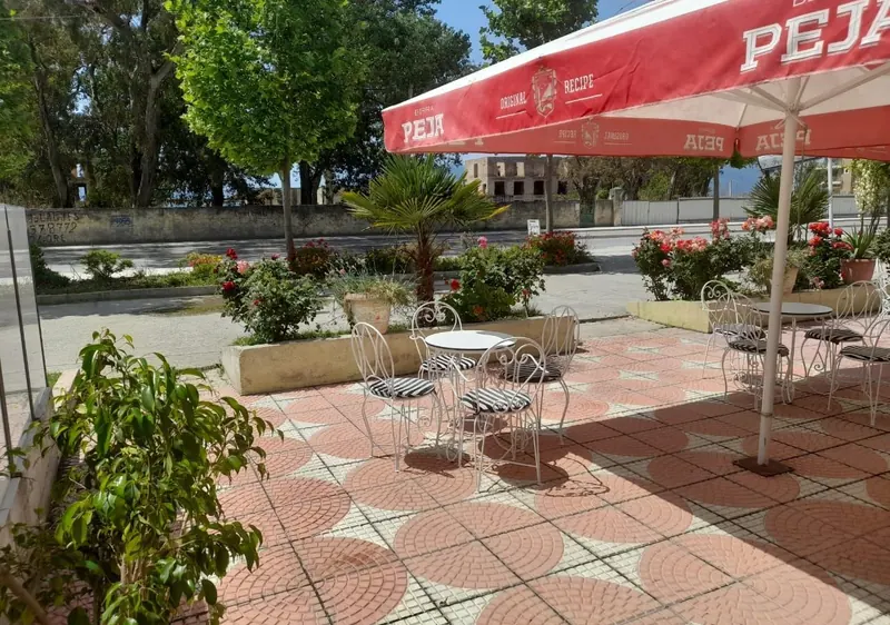 Bistro tables under a red umbrella on the tiled terrace, flowers and palms along the street