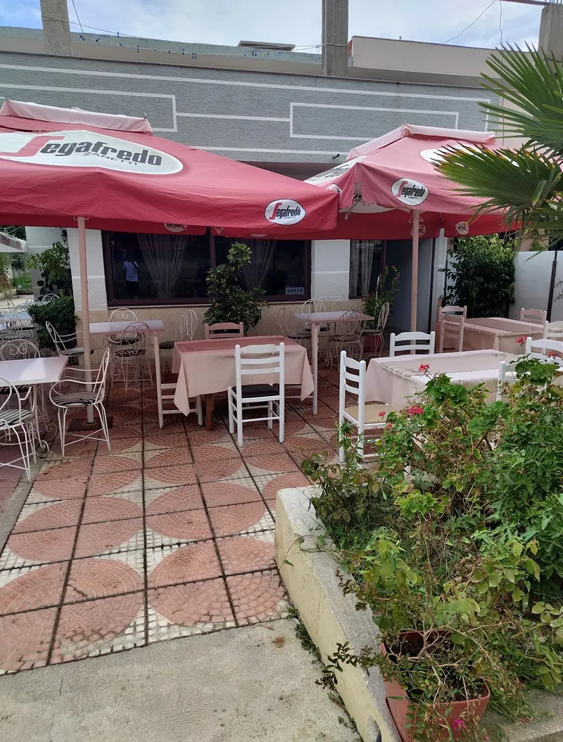 Tables with pink cloths under red umbrellas, a planter of greenery in front